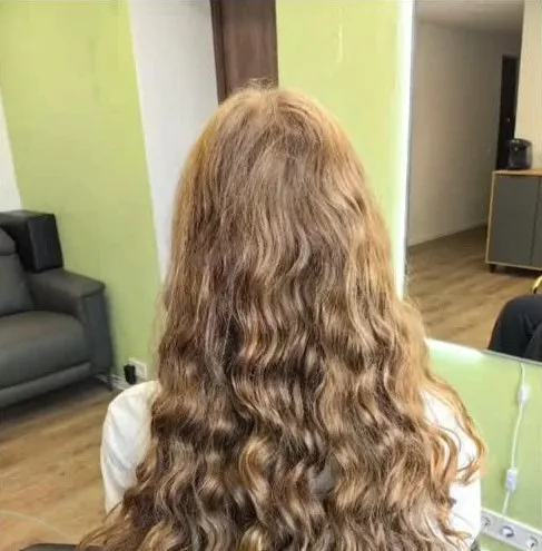 Gari gaiši brūni mati ar cirtām, klientei sēžot salona krēslā